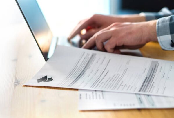 Young man writing college or university application form with laptop. Student applying to school. Scholarship document, admission paper or letter on table. Typing email. Education and communication.